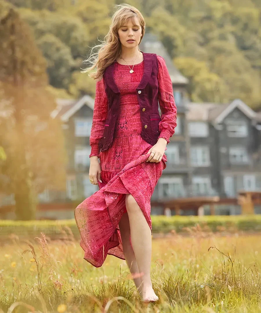 The Freya waistcoat worn over a pink dress in a meadow