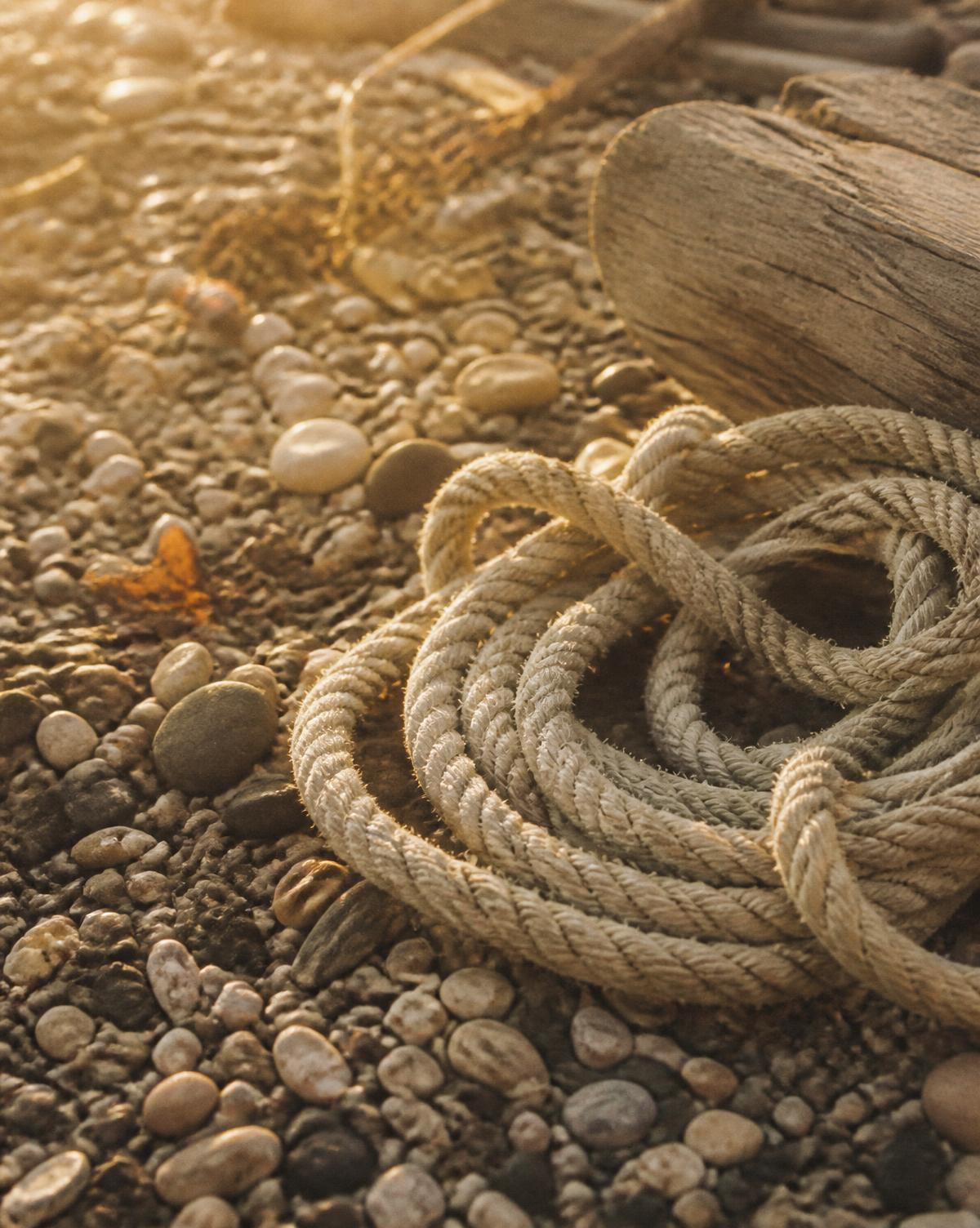 Close view of sun-bleached shingle pebbles and a coil of weathered rope on the beach at golden hour